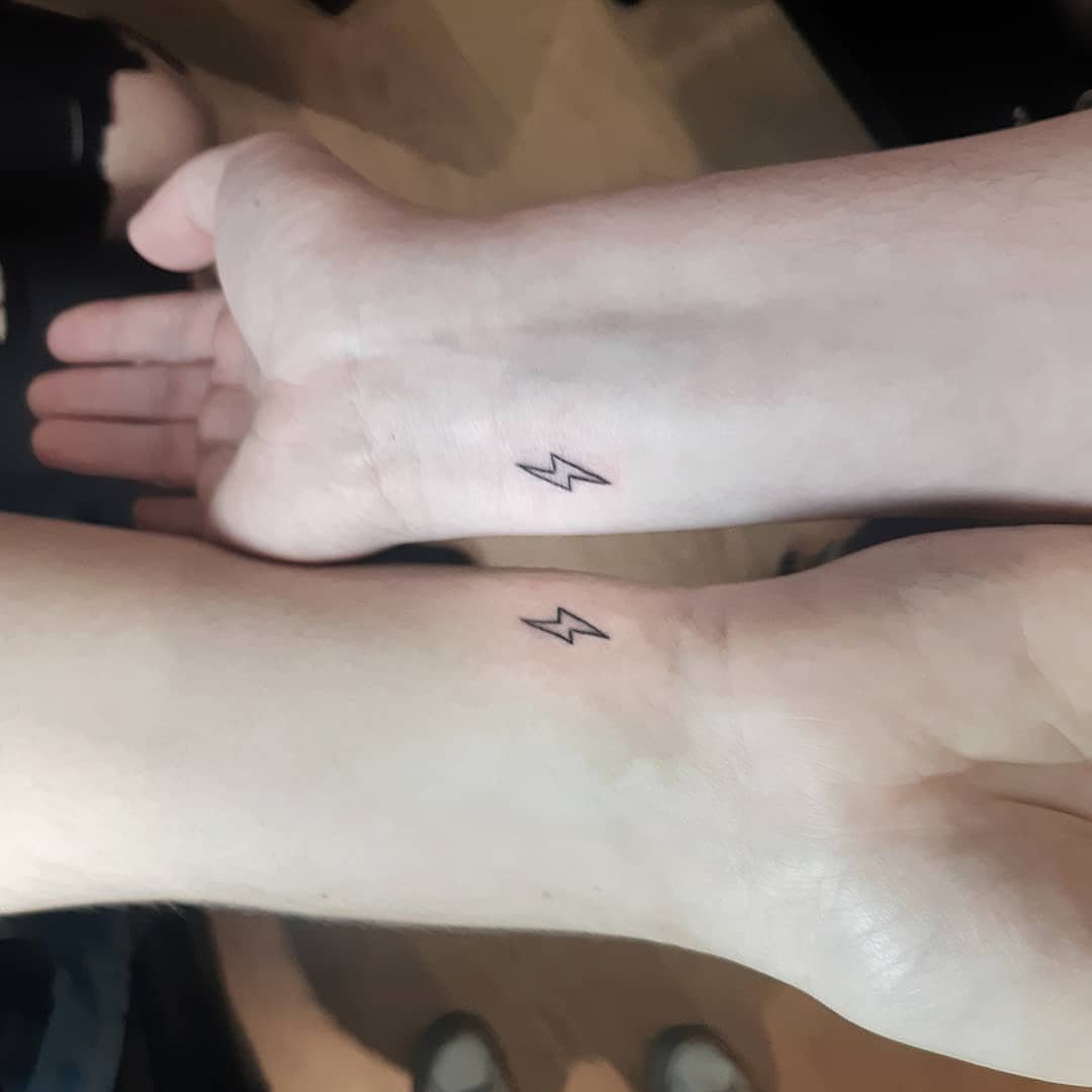 Two inner wrists with matching small black lightning bolt tattoos side by side.