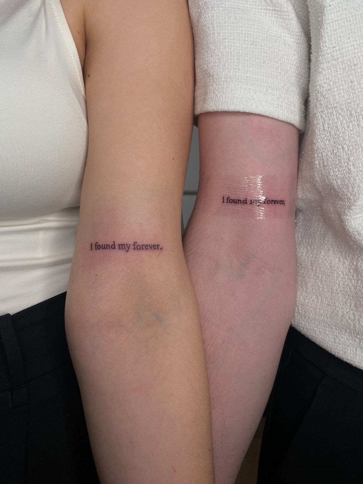 Two forearms with matching tattoos reading I found my forever in fine script.