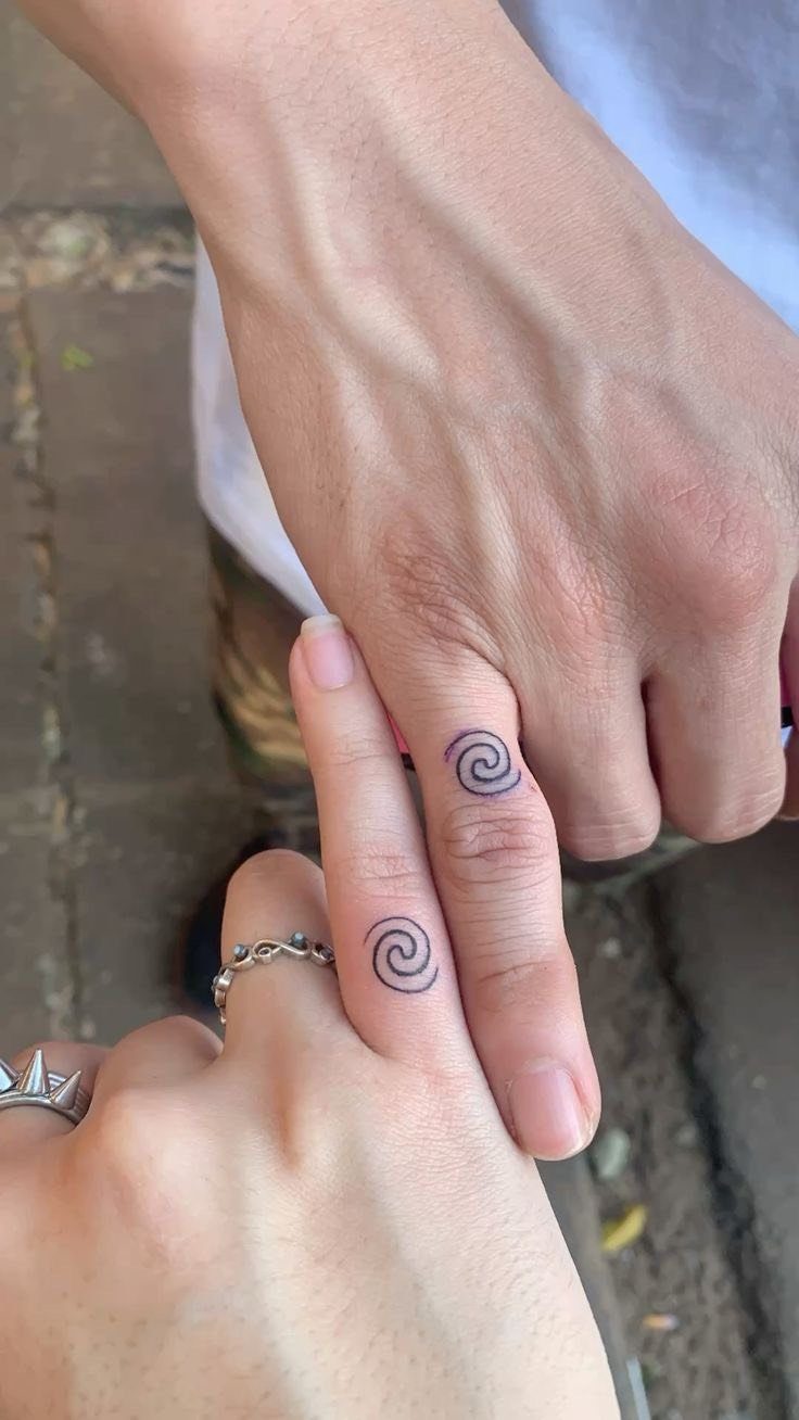 Two fingers with matching small black spiral tattoos held side by side.