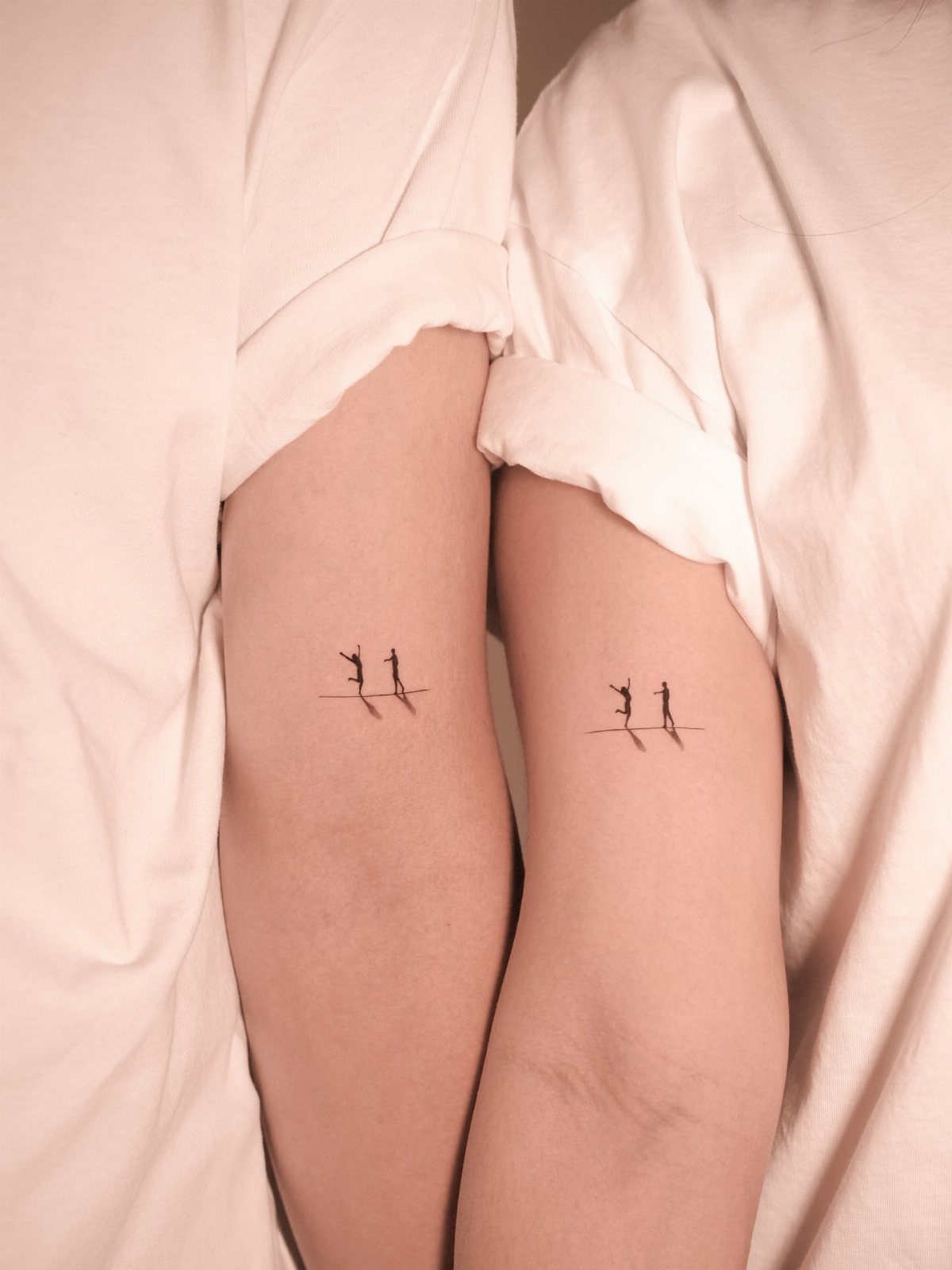 Matching stick figure tattoos on the inner forearms of two people wearing white shirts.