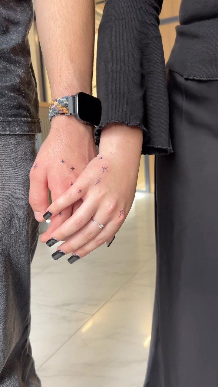 Two people holding hands with matching small star tattoos on their fingers