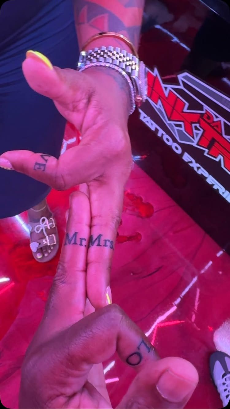 Intertwined hands showing matching Mr. and Mrs. finger tattoos in a studio.