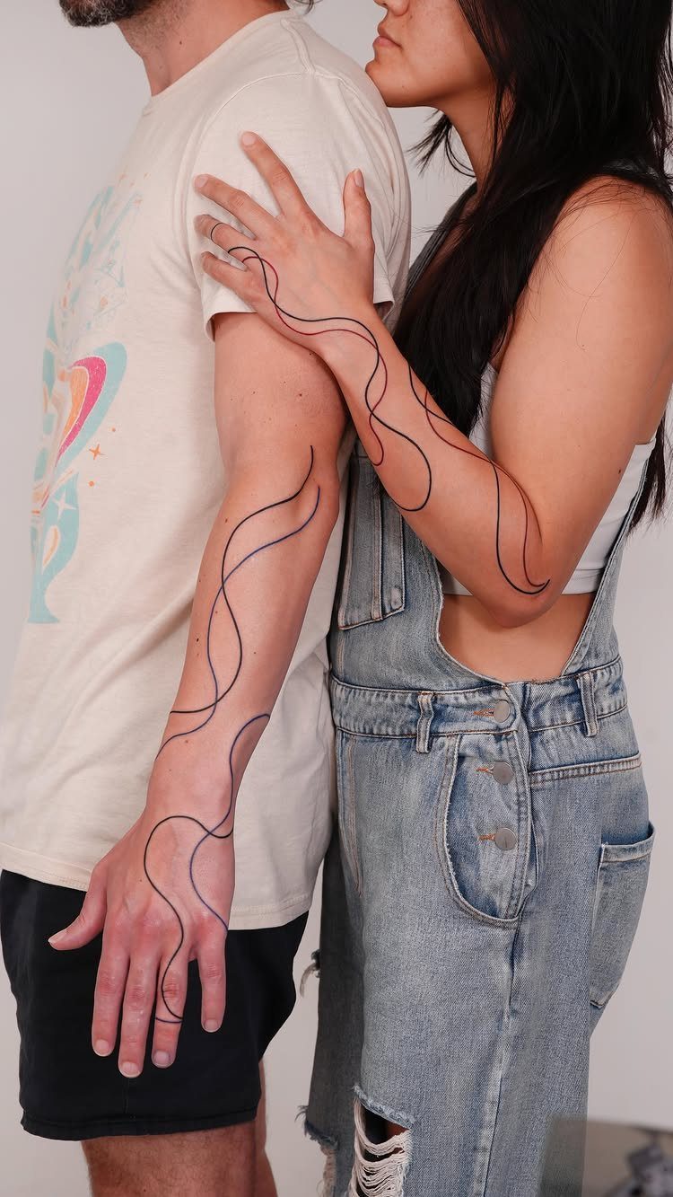Couple with matching flowing abstract line tattoos on their forearms standing together.