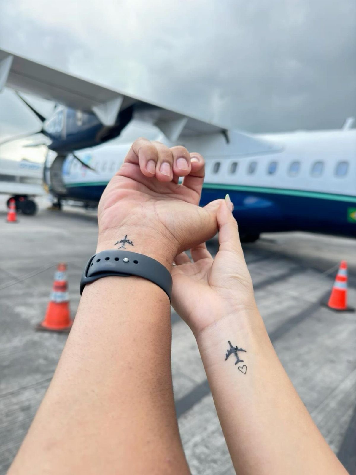 Two wrists with matching small airplane tattoos held together in front of a plane.