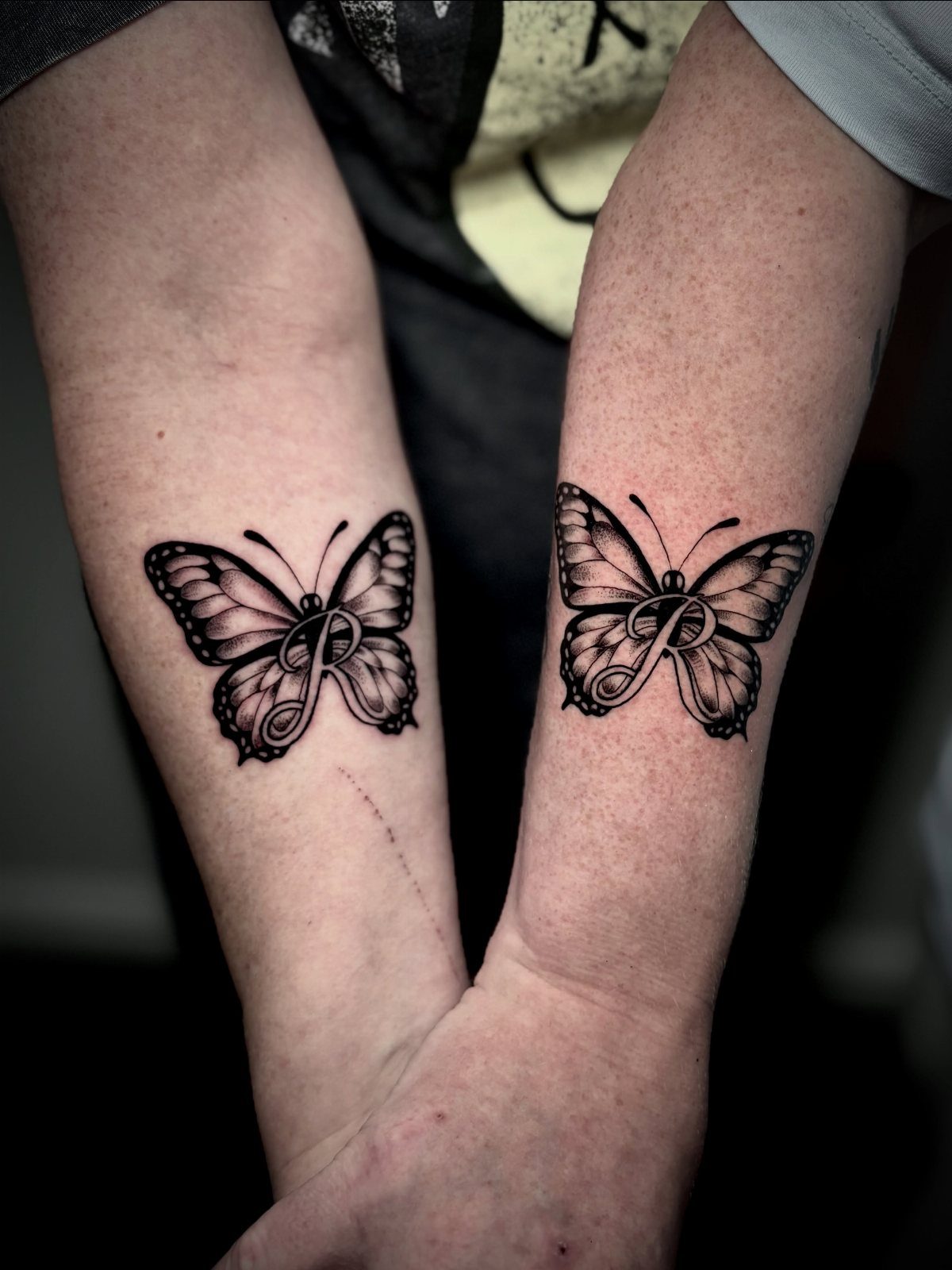 Matching butterfly tattoos on two forearms with a stylized letter P inside