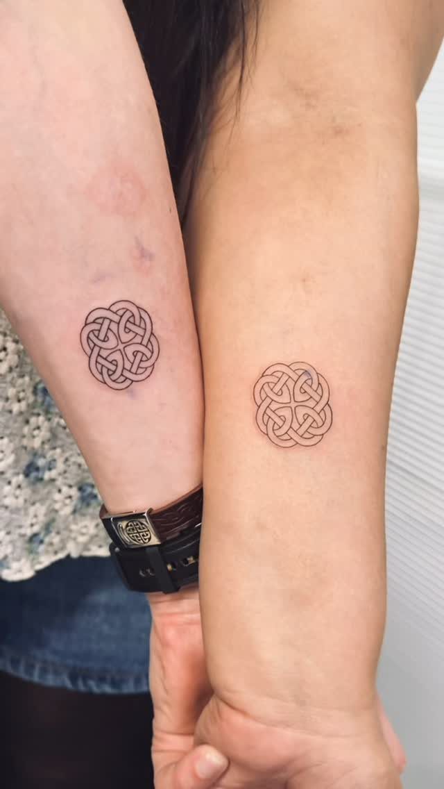 Matching Celtic knot tattoos on the forearms of two people standing side-by-side.