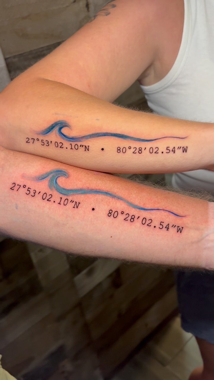 Matching forearm tattoos of a blue wave and geographic coordinates on two people