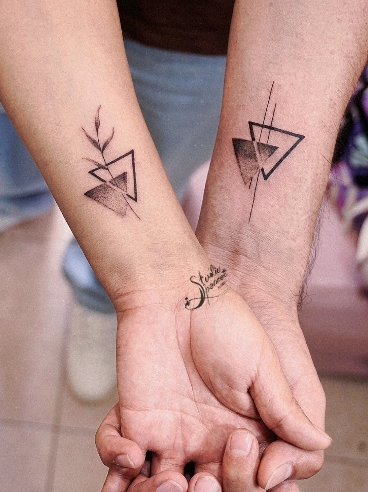 Matching geometric triangle tattoos on the inner forearms of a couple holding hands.
