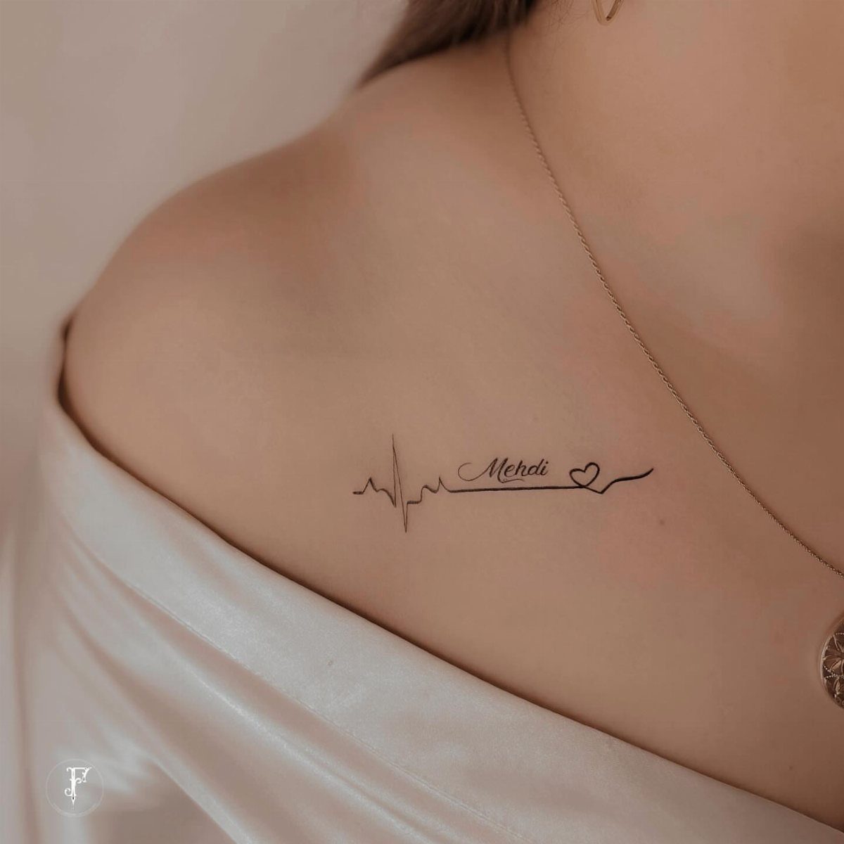 Heartbeat line tattoo with the name Mendi and a heart on a collarbone