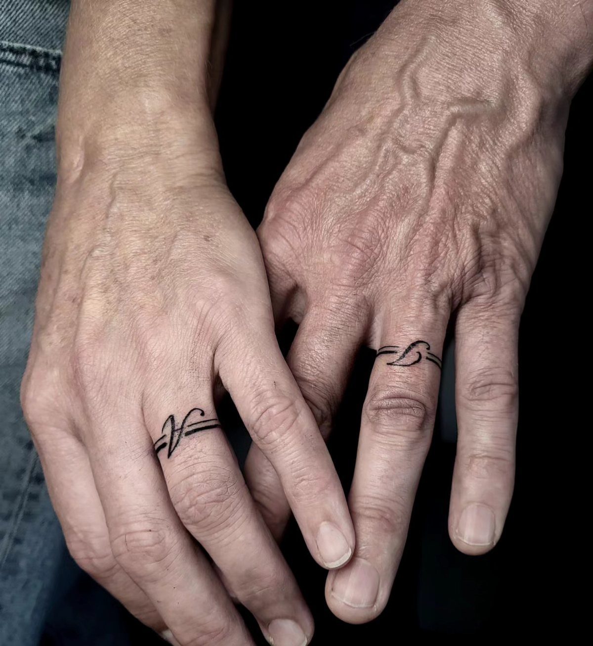 Two hands with matching ring finger tattoos featuring the initials A and S.