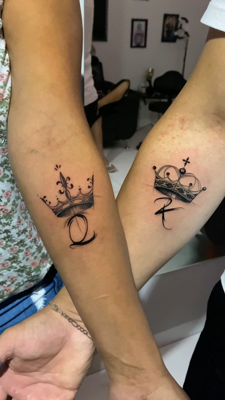 Two forearms with matching king and queen crown tattoos including letters K and Q.