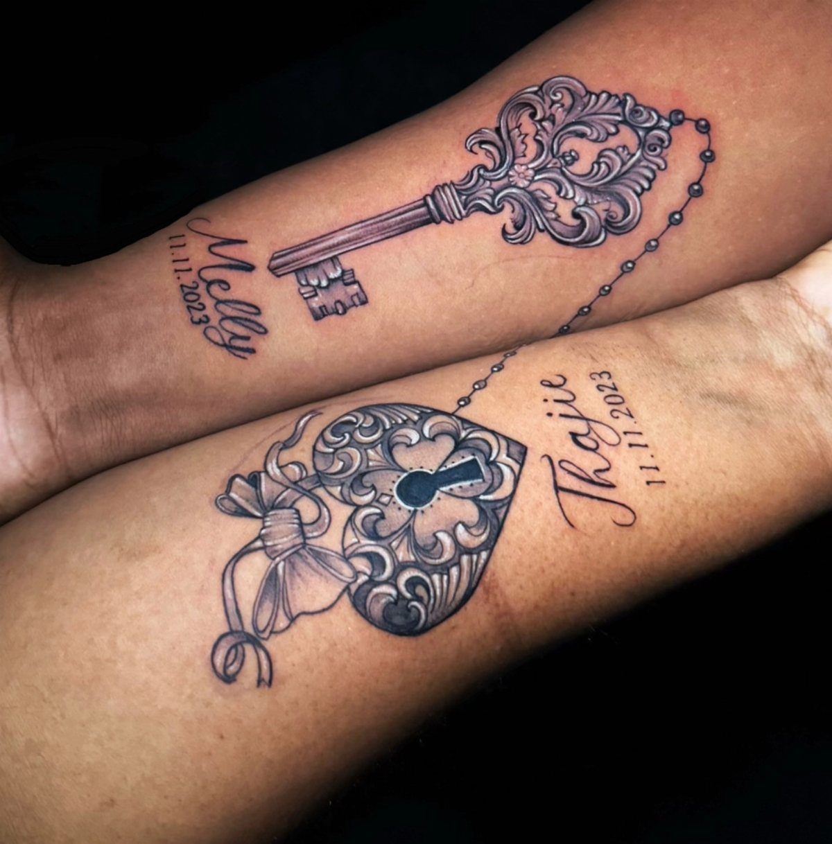 Matching ornate lock and key tattoos on two forearms with names and dates.