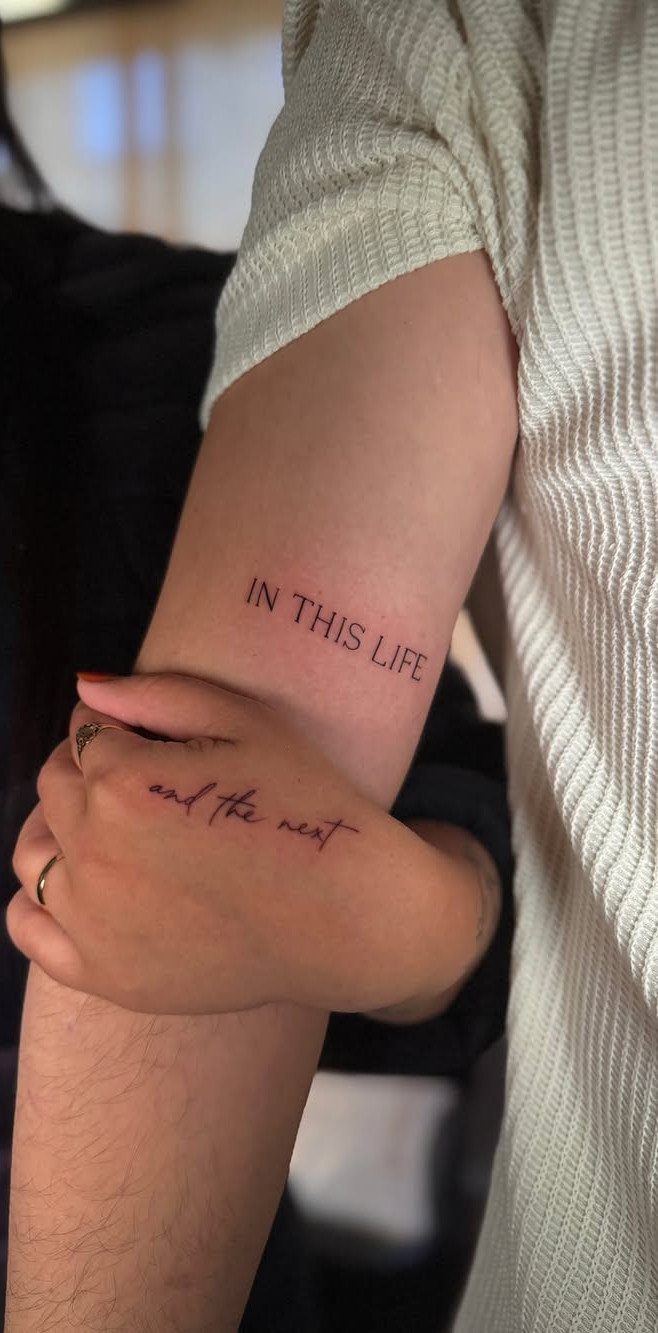 Matching couple tattoos on arms reading 'IN THIS LIFE and the next' in text.