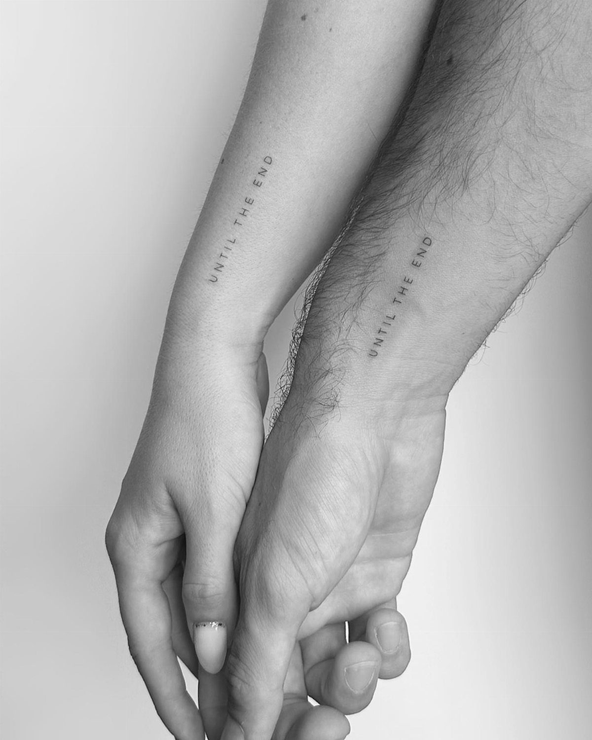 Two people holding hands with matching Until The End wrist tattoos