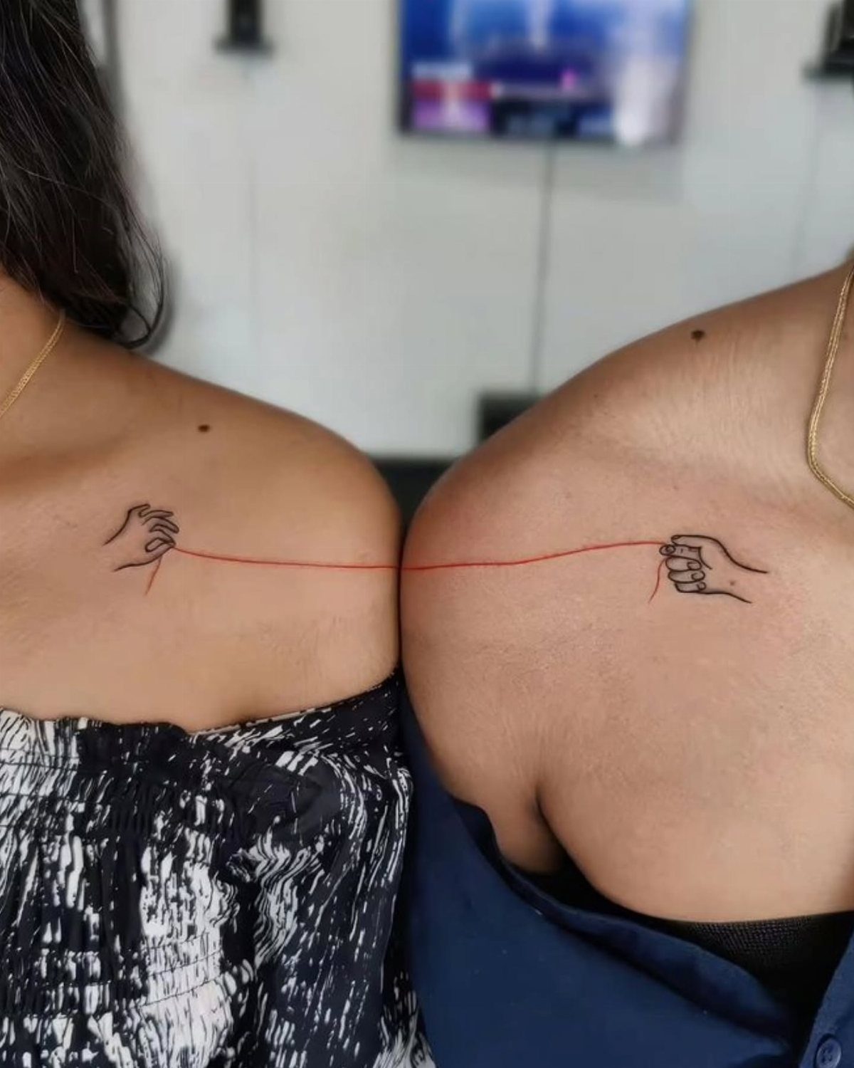 Two people with matching shoulder tattoos of hands connected by a red line.