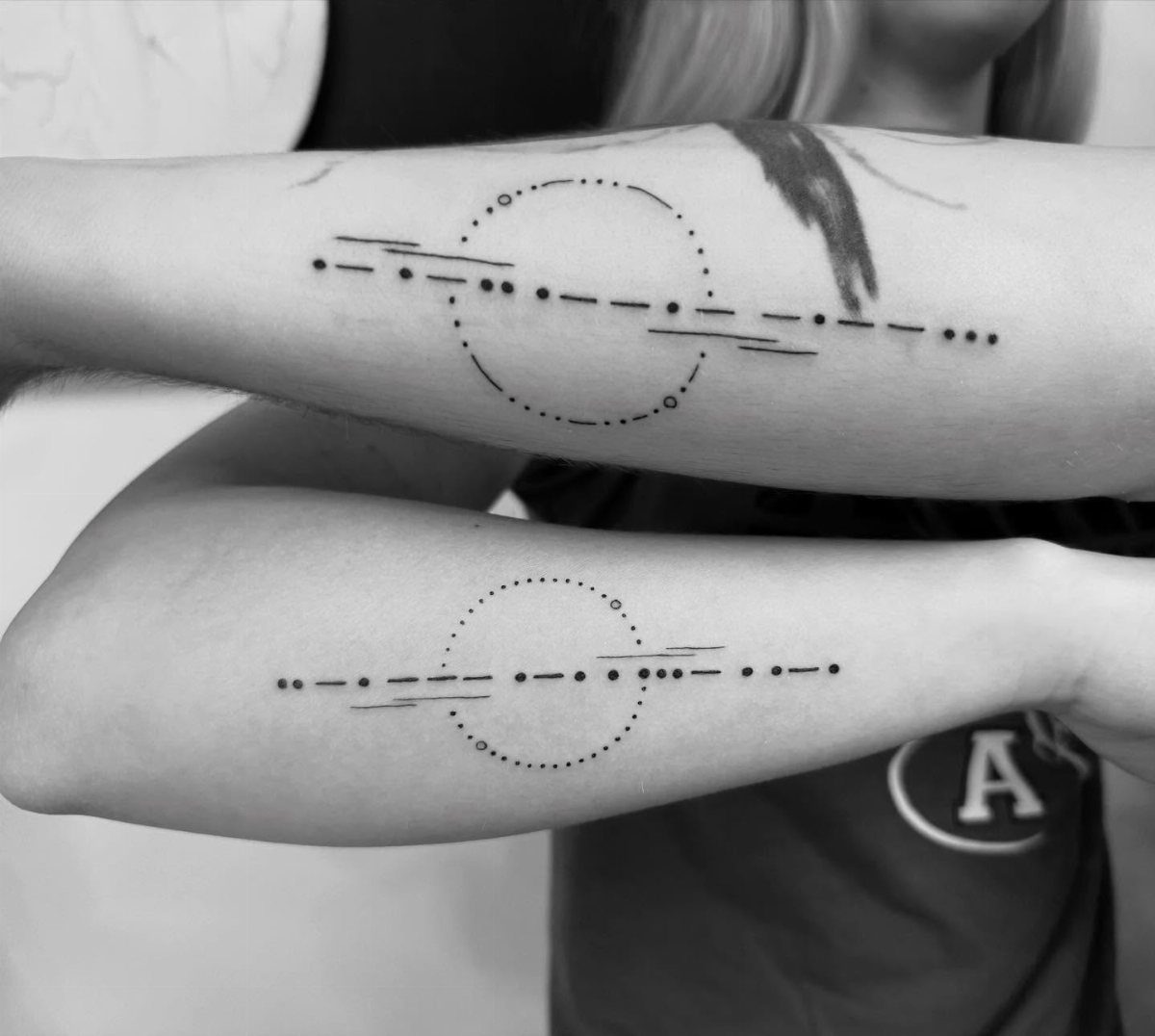 Matching tattoos on two forearms featuring dotted circles and linear morse code patterns.
