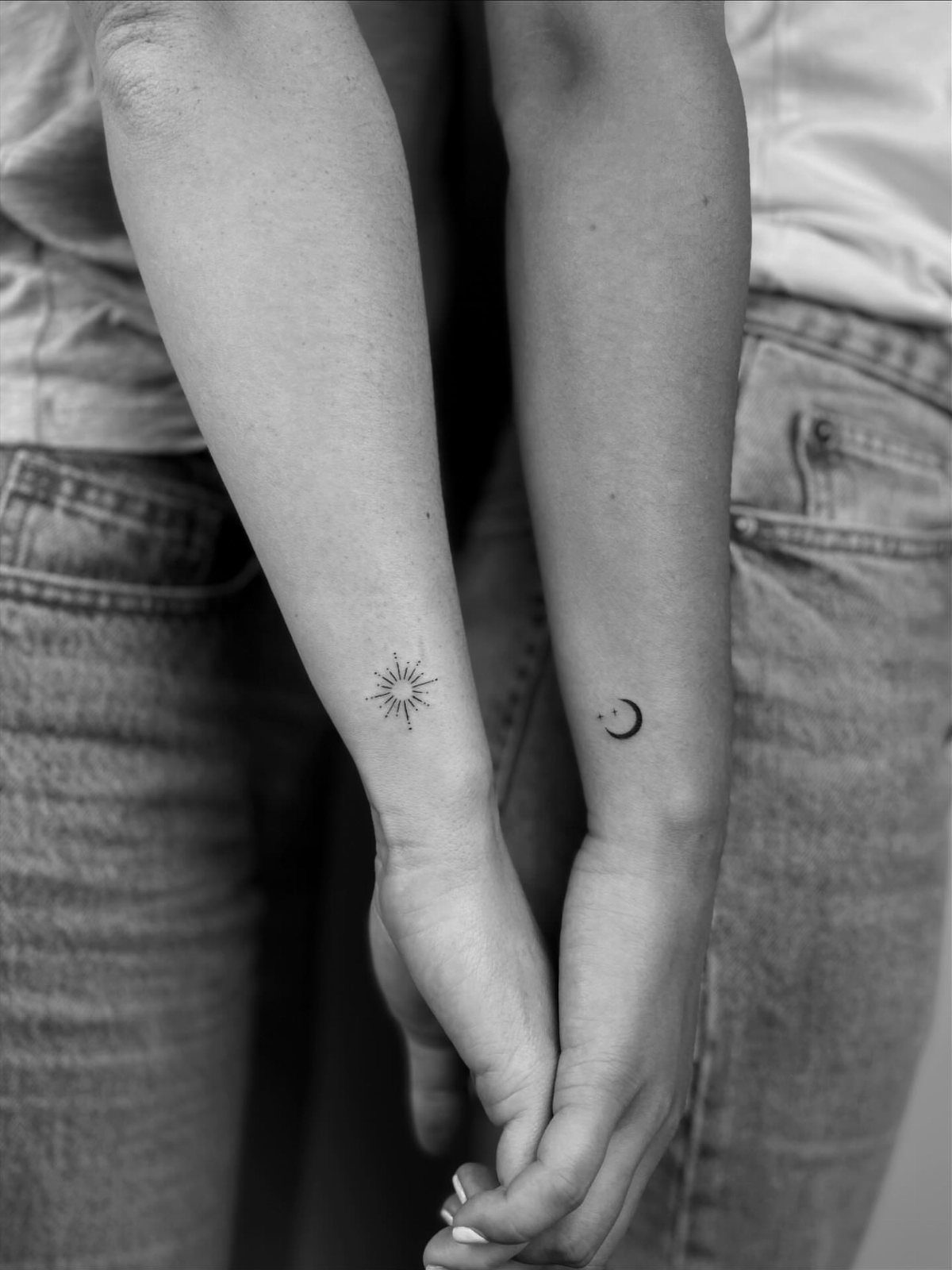 Two inner wrists featuring matching small sun and crescent moon tattoos in black ink.