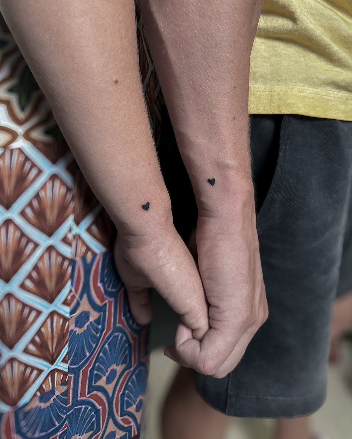 Two wrists side-by-side each featuring a small solid black heart tattoo.