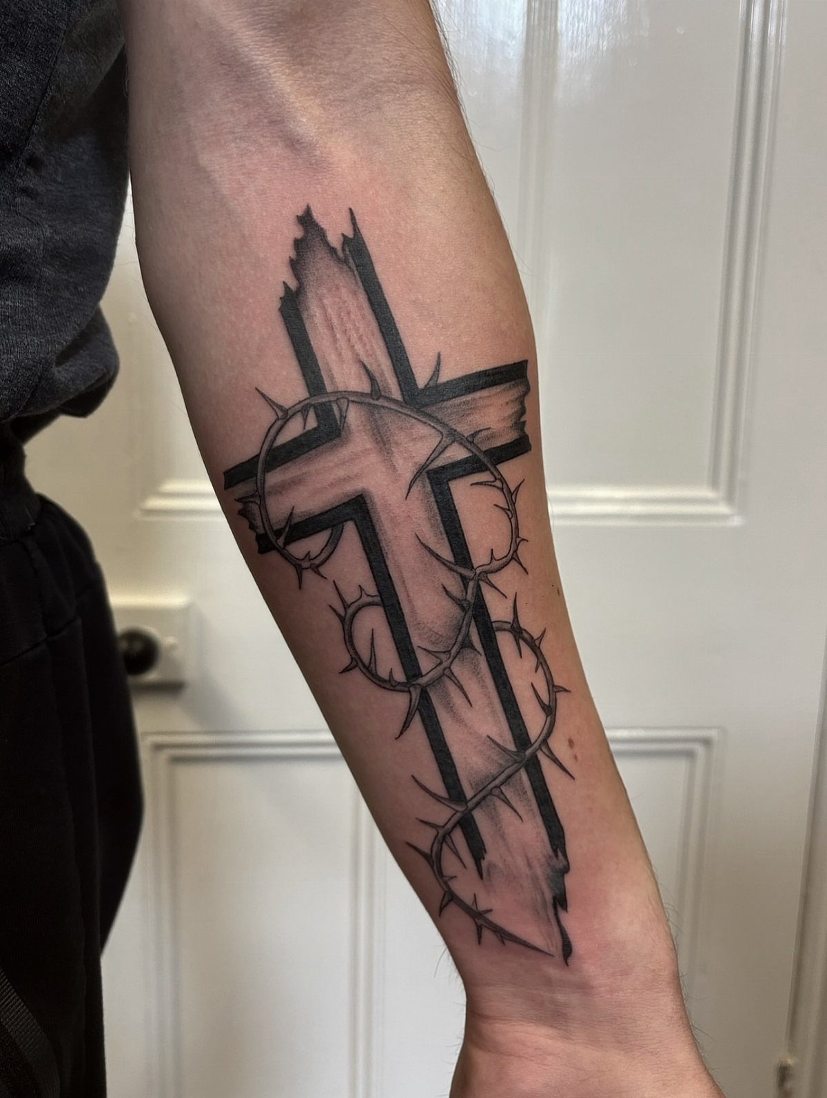 Cross tattoo wrapped in barbed wire on a person's forearm