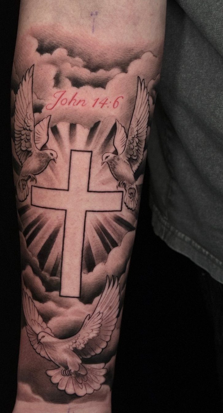 Forearm tattoo of a cross with doves, clouds, and red scripture text.