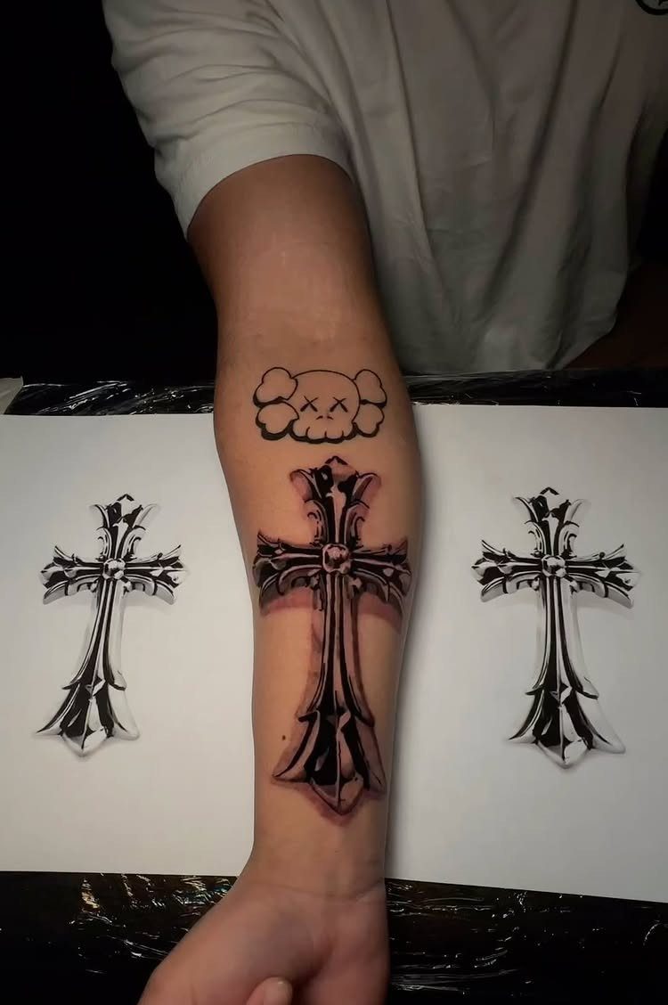 Ornate filigree cross tattoo on a forearm with design sketches nearby