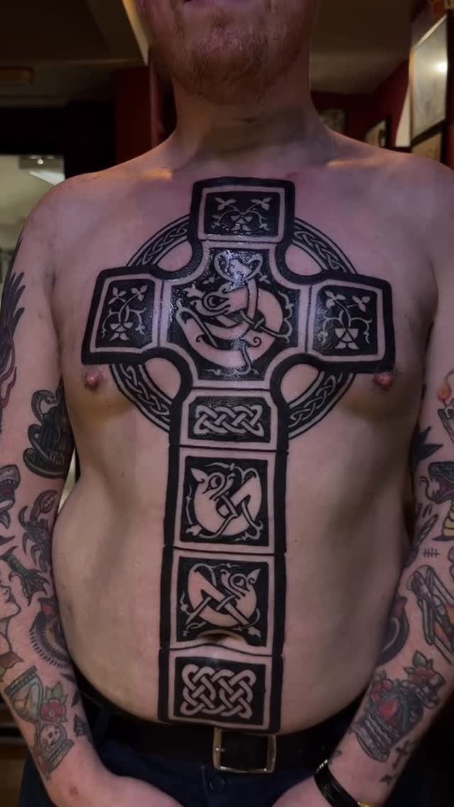 Large black Celtic cross tattoo with intricate knotwork on a man's chest and torso