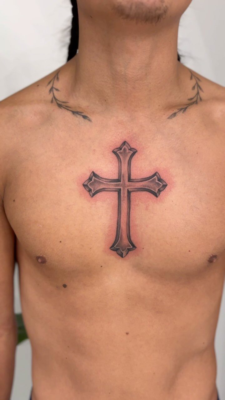 Ornate grey cross tattoo with red shading centered on a man's chest