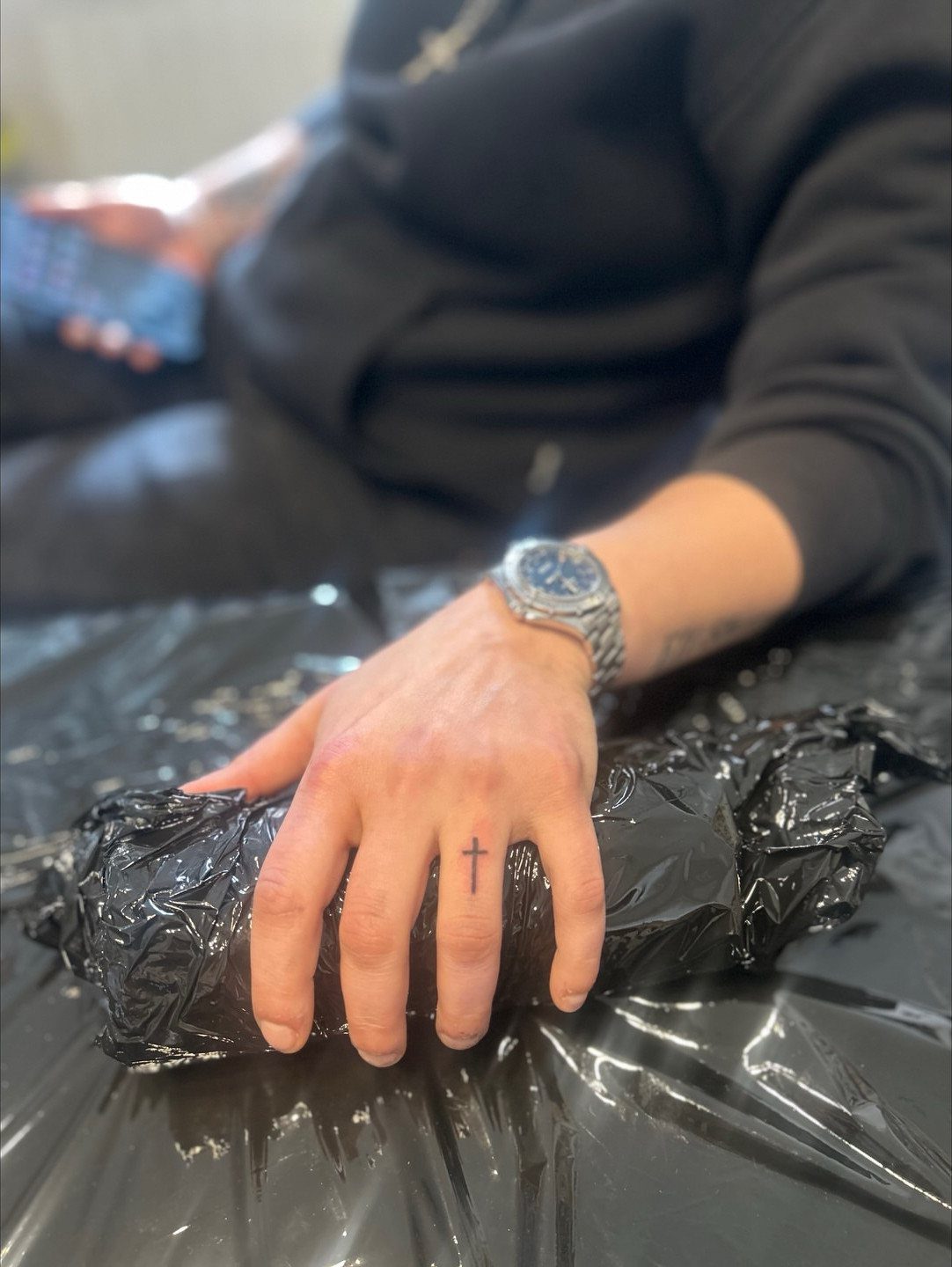 Man's hand with a small black cross tattoo on the middle finger