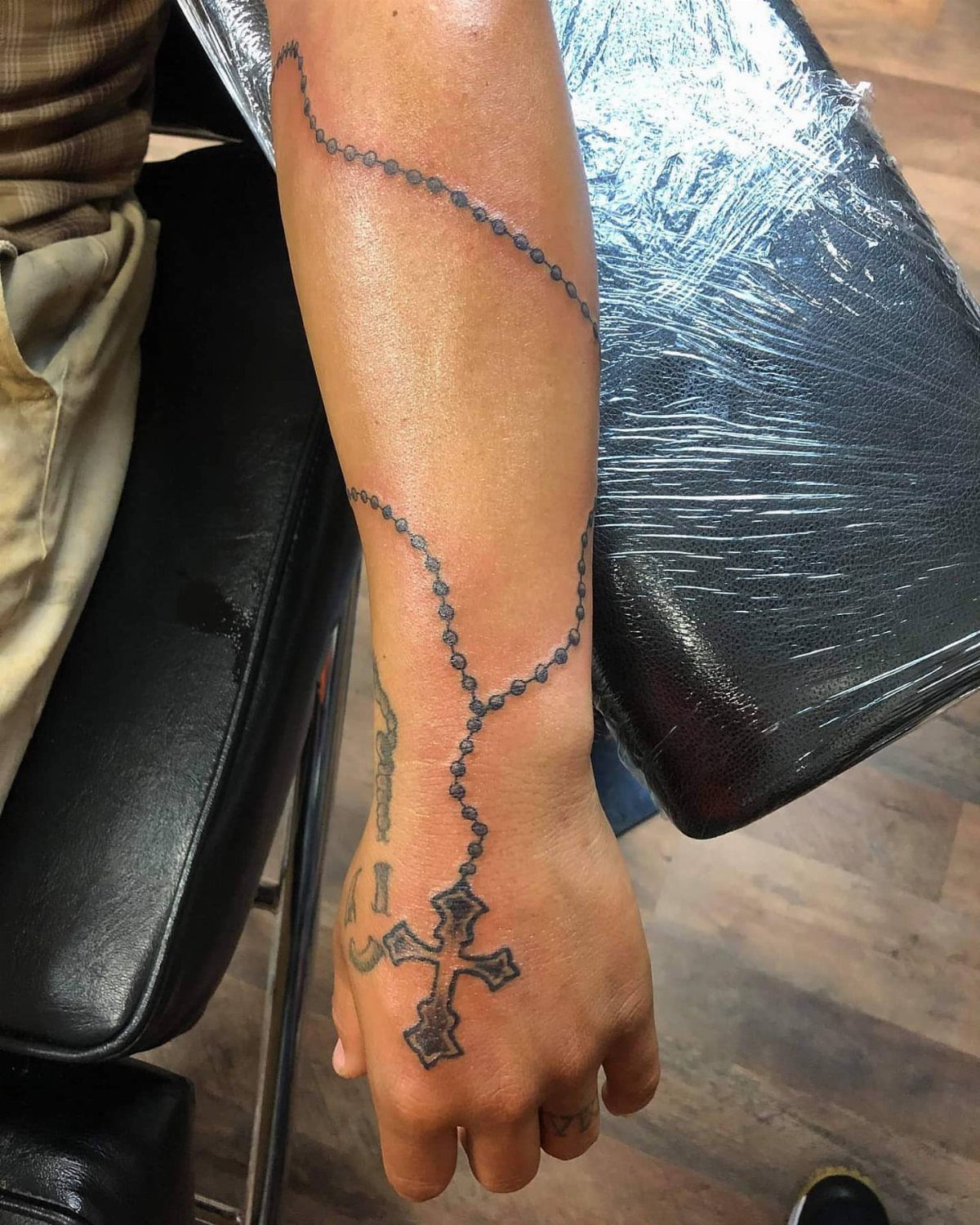 Rosary bead tattoo wrapping around a forearm and ending in a hand cross.