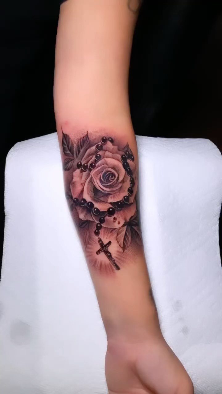 Forearm tattoo of a realistic rose entwined with a rosary and cross