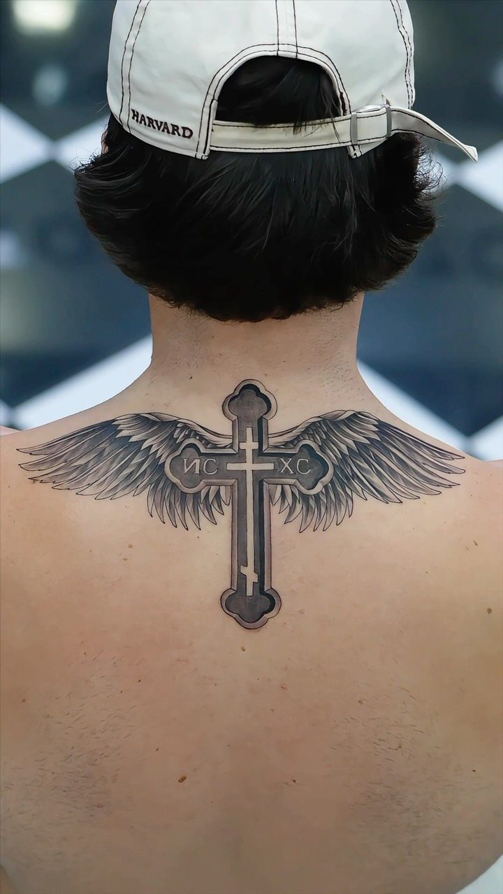 Orthodox cross tattoo with large angel wings on a man's upper back