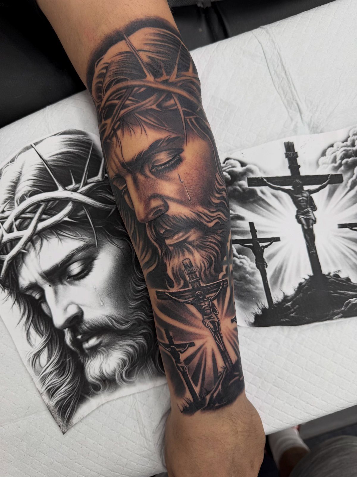 Detailed black and grey forearm tattoo of Jesus and three crosses with reference art.