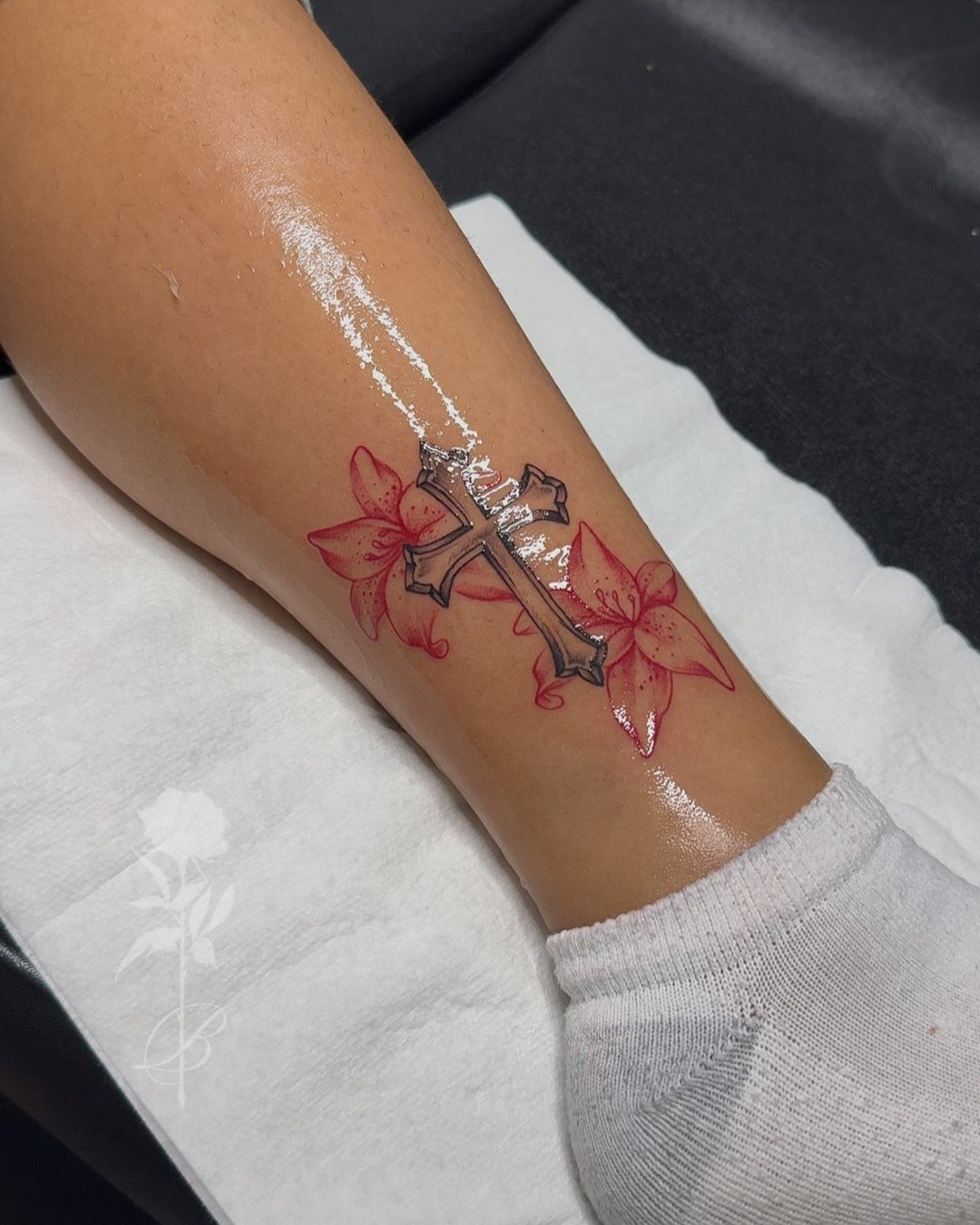 Tattoo of a grey stone cross with red lily flowers on a wrist