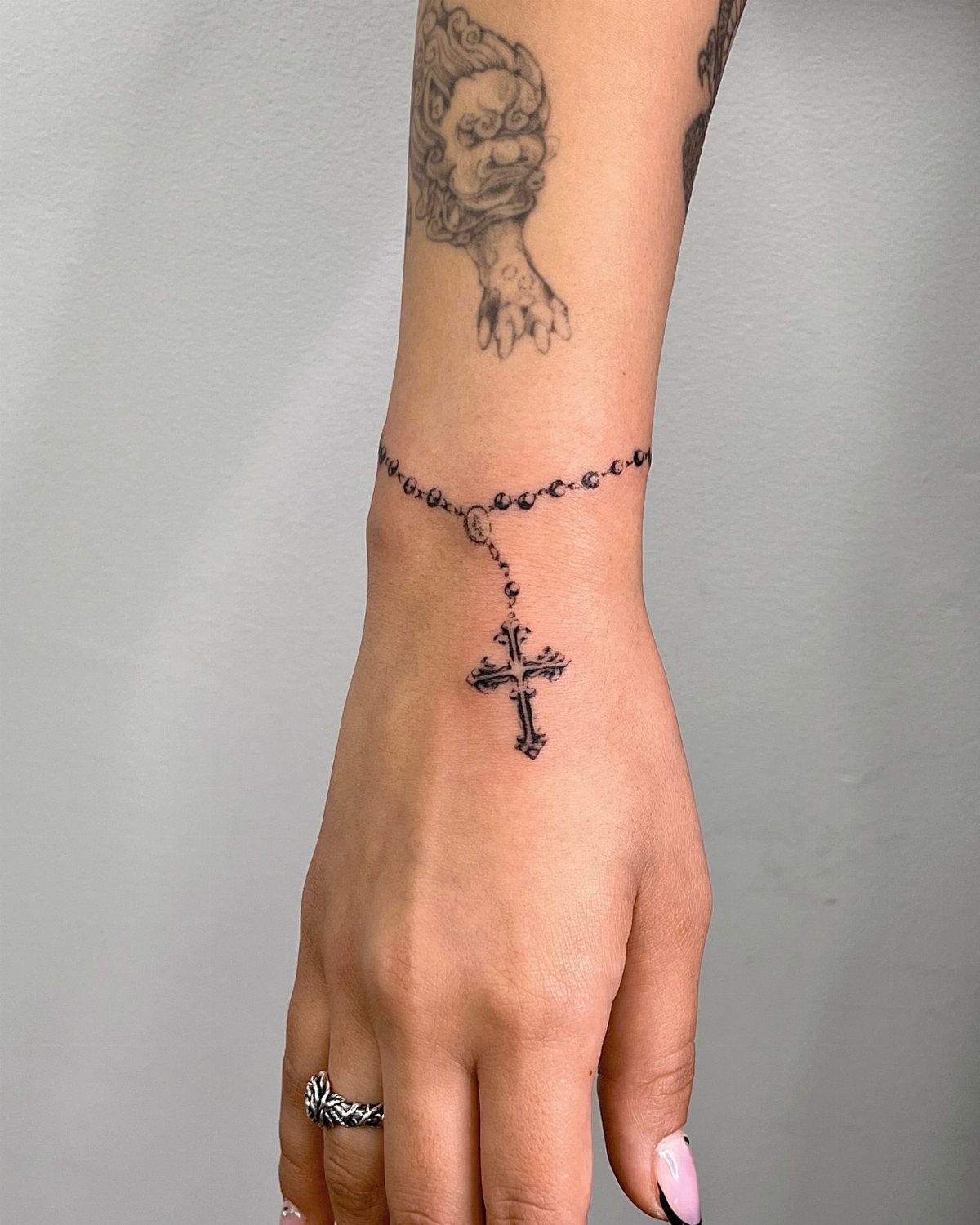 Cross bracelet tattoo on a wrist with a beaded rosary design and hanging cross