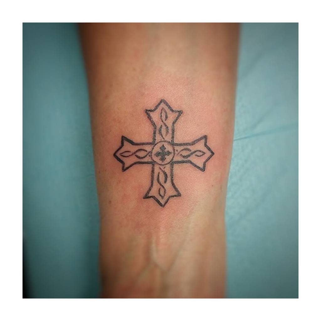 Celtic style black ink cross tattoo centered on a person's inner wrist