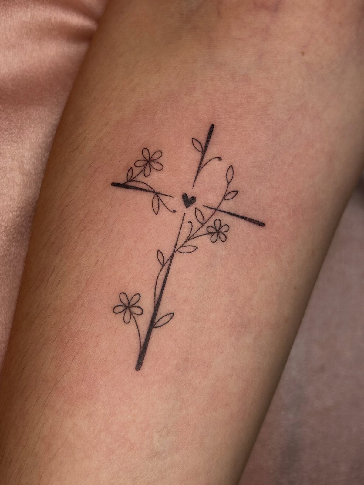 Black ink cross tattoo entwined with a floral vine and small heart