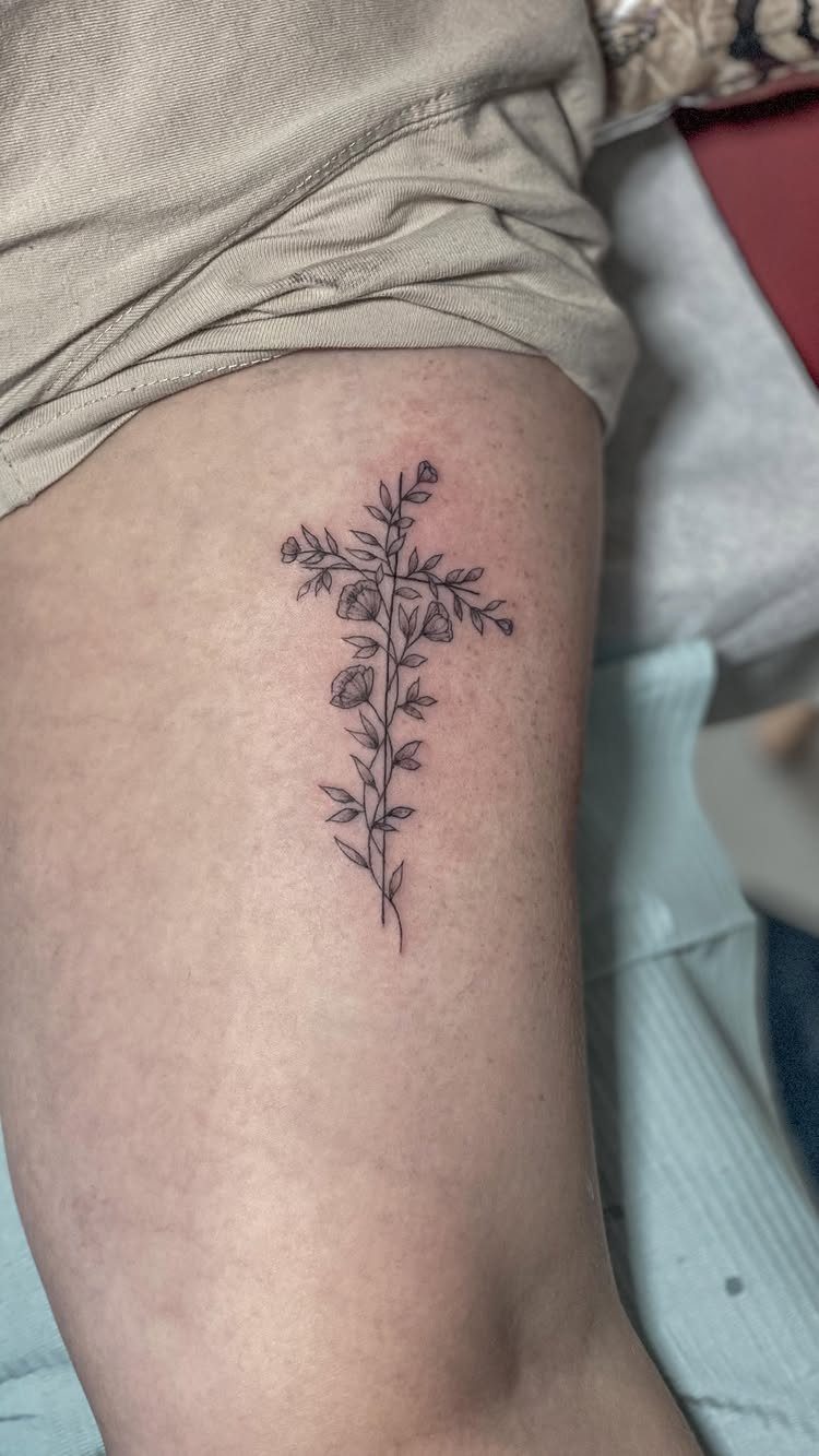 Floral cross tattoo with delicate vines and small flowers on a lower leg