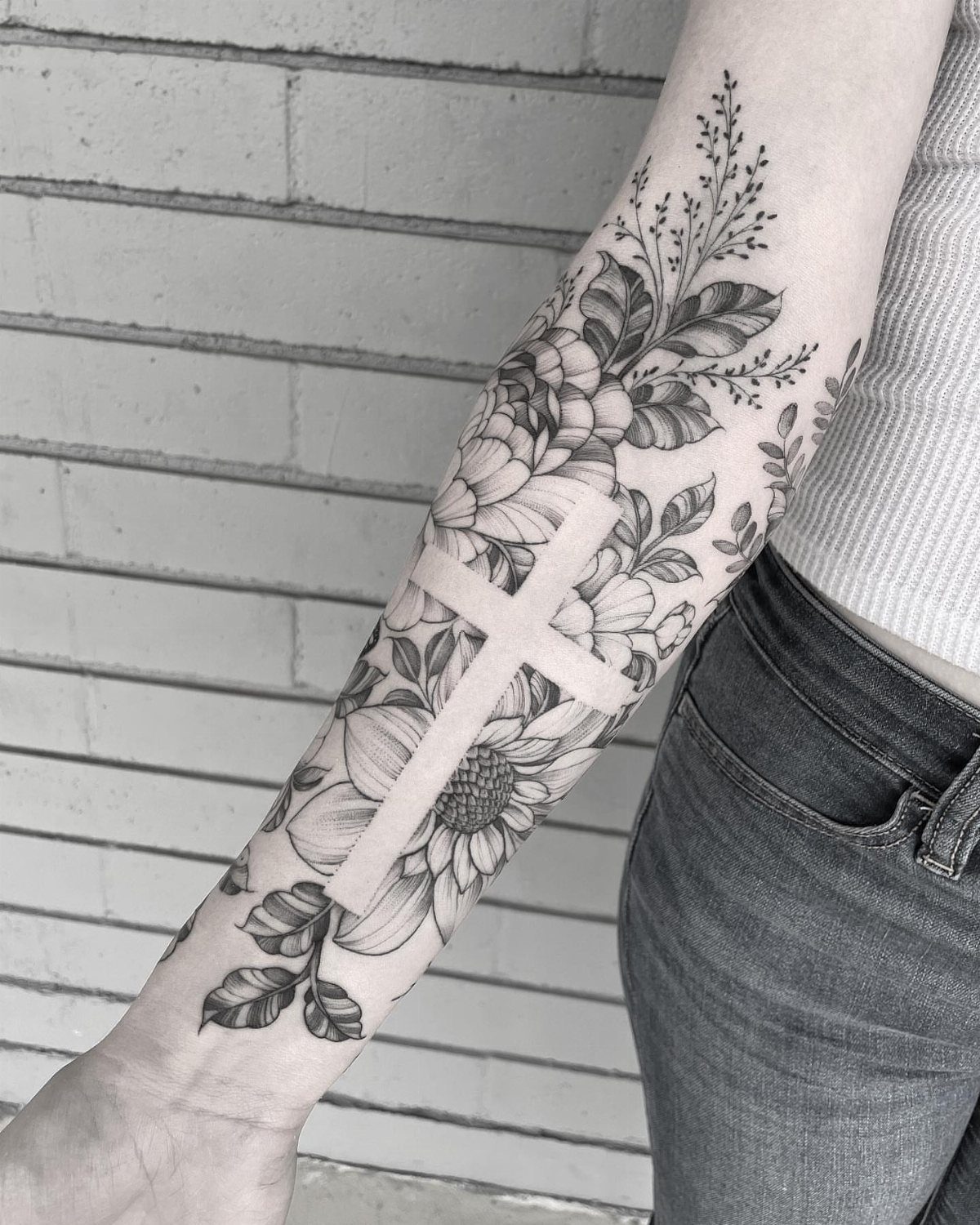 Floral tattoo on a forearm featuring a negative space cross and sunflowers.