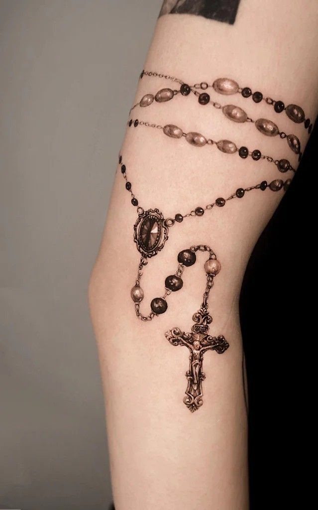 Ornate rosary tattoo with beads and a crucifix on a person's arm