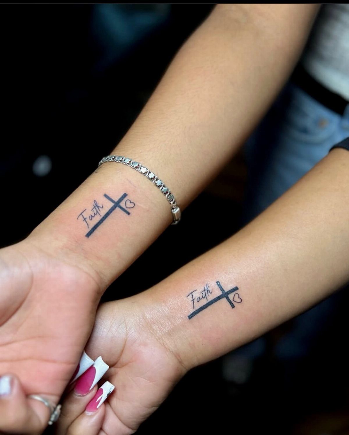 Two wrists with matching black ink cross tattoos entwined with the word Faith.