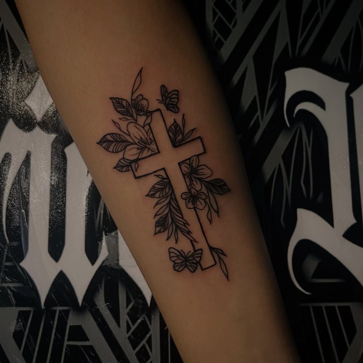 Black ink cross tattoo with flowers and butterflies on a person's arm
