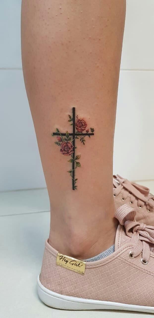 Tattoo of a black cross with red roses on a person's ankle