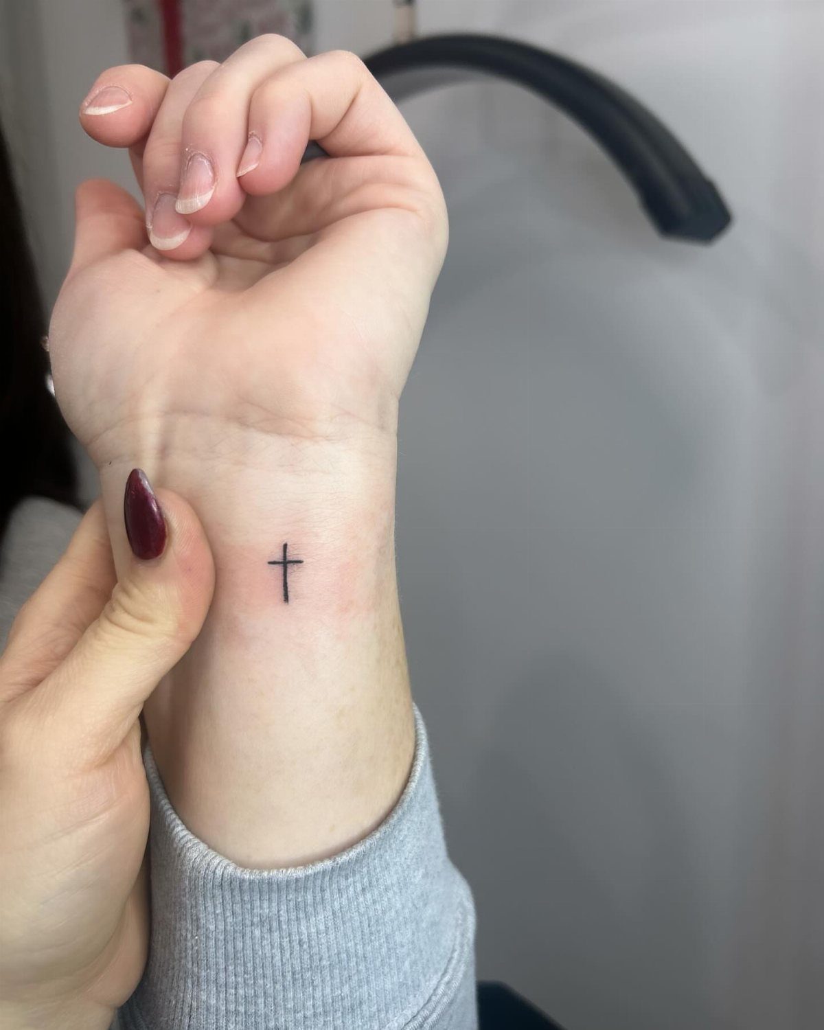 Small thin black ink cross tattoo centered on a person's inner wrist