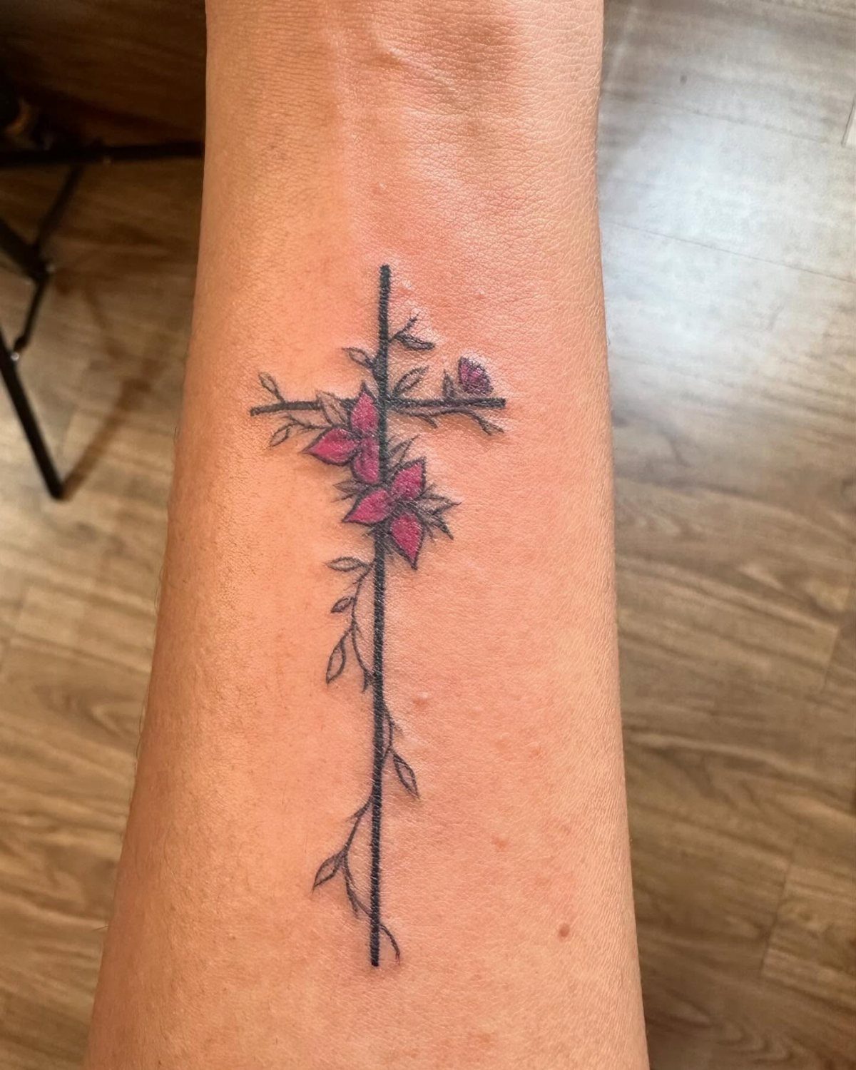 Purple floral cross tattoo with a thin black vine on a forearm