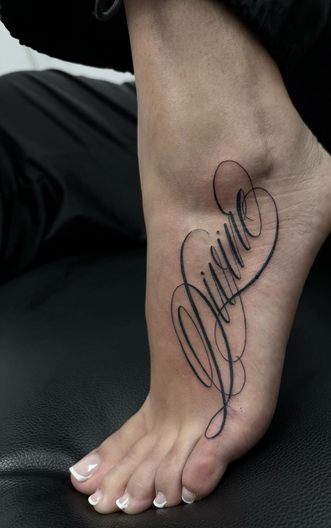 Cursive tattoo with looping black script lettering on the side of a foot.