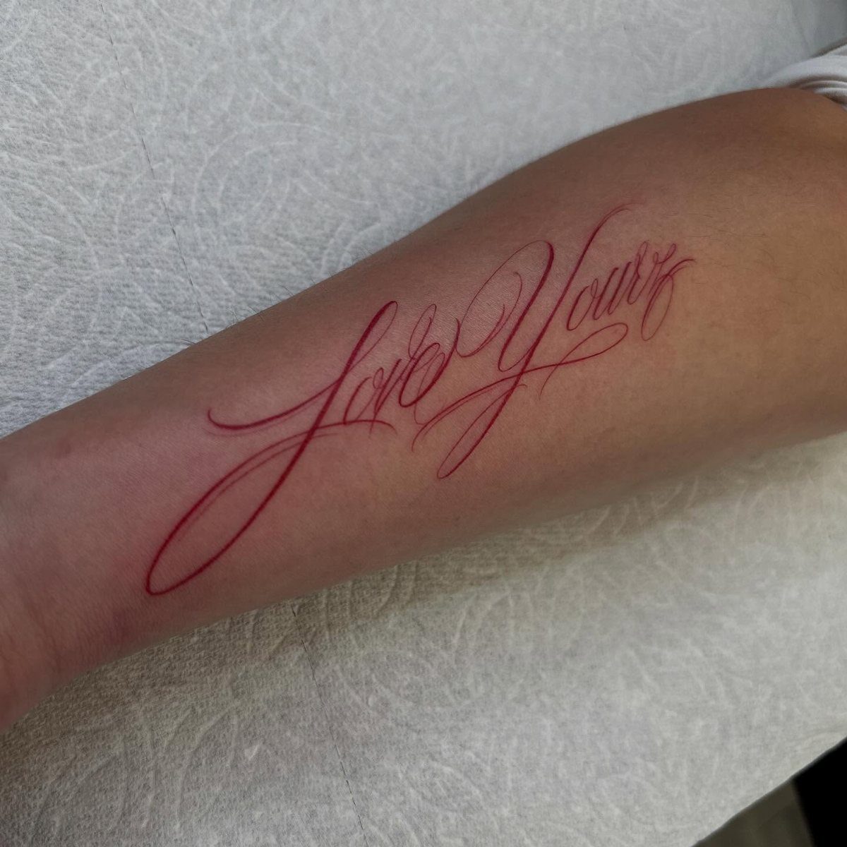 Red cursive tattoo reading Love Yours on a person's forearm