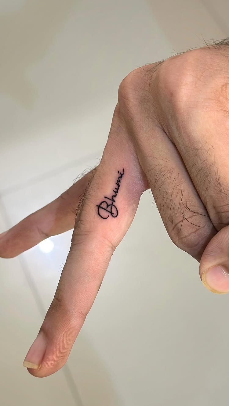 Cursive name tattoo reading Bhumi on the side of a person's finger