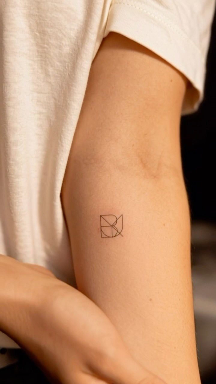 Geometric monogram tattoo on the inner upper arm of a person