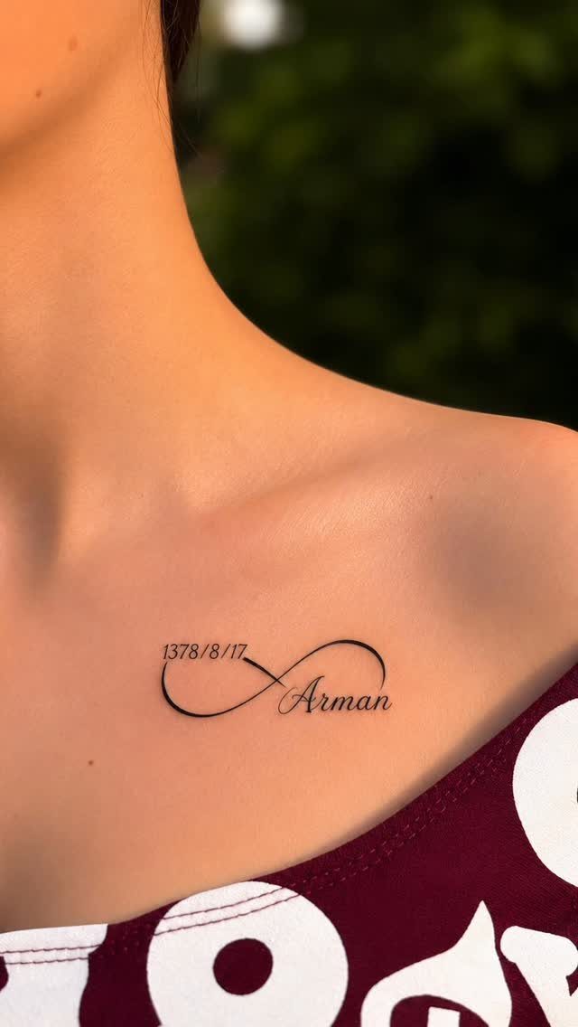 Infinity symbol tattoo with the name Arman and a date on a collarbone