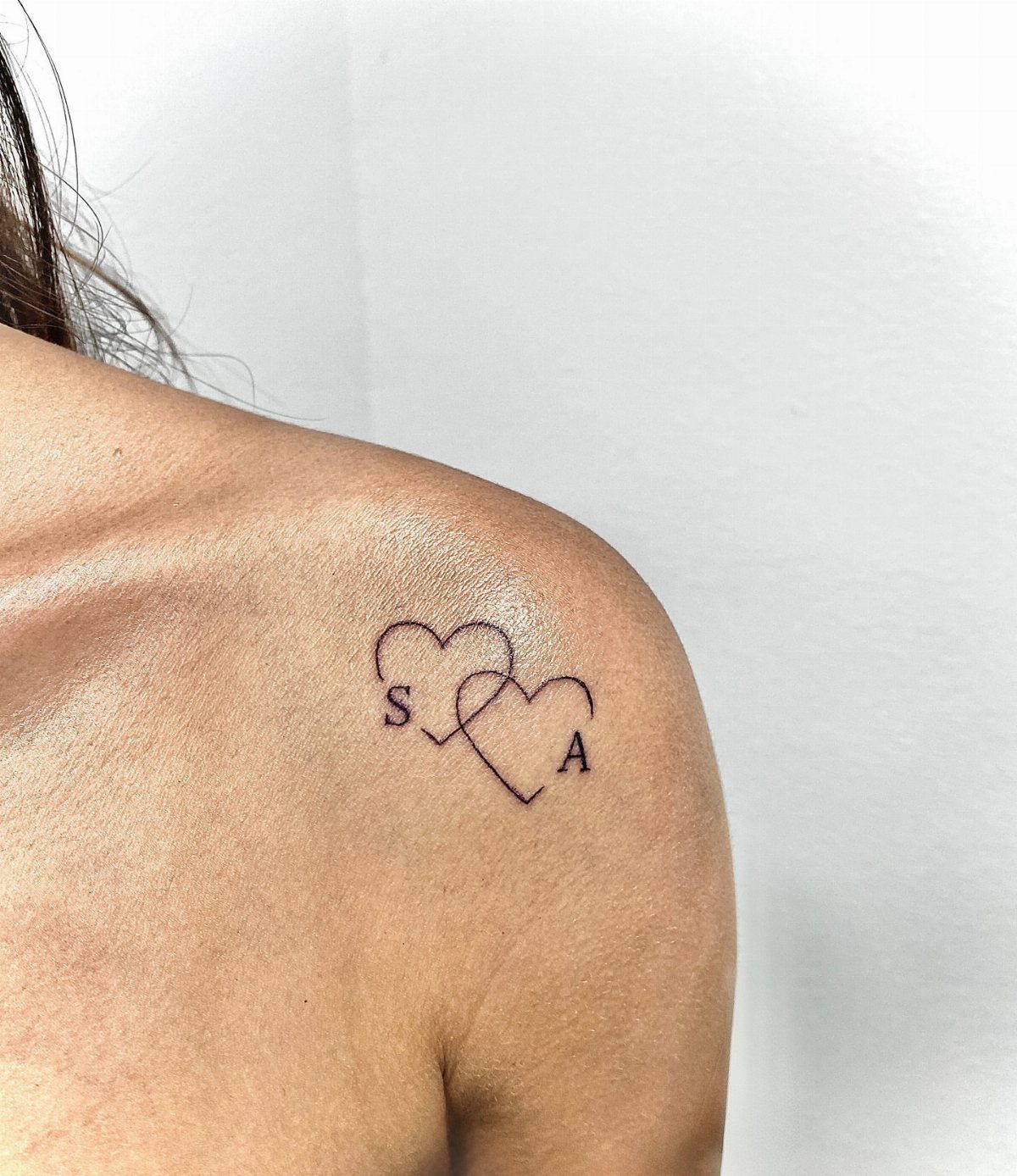 Interlocking heart tattoo on a shoulder with initials S and A inside.
